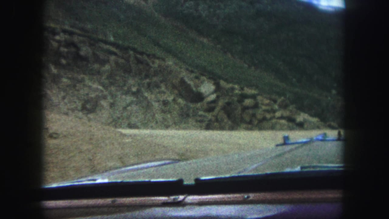 1958 Colorado Springs home-movie frame looking through a car windshield toward a mountain road and rocky hillside.