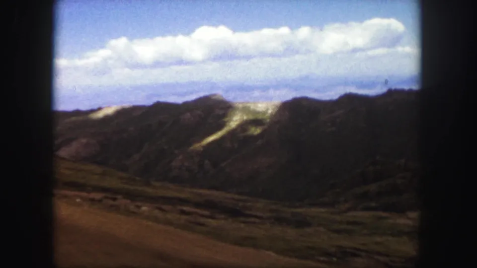 1958 Colorado Springs travel footage frame with a broad mountain ridge, light-colored slope streaks, and a cloud-filled sky.
