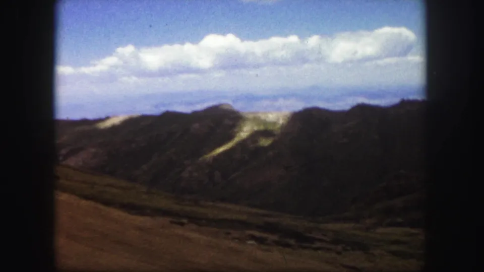 1958 Colorado Springs 8mm frame showing layered mountain slopes, rocky ground, pale hillside marks, and soft film borders.