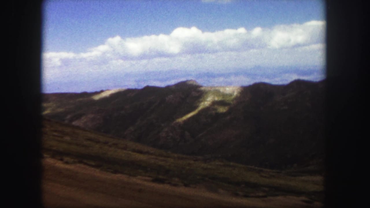 Mountain ridgeline and cloud-filled sky framed by dark film borders.