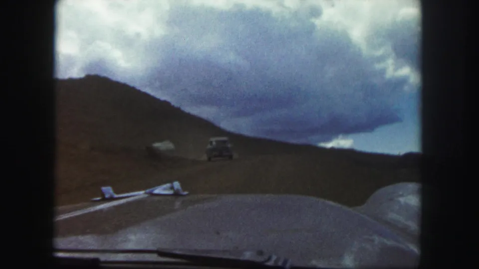 Dashboard-level 1958 Colorado Springs road view follows a classic car along an unpaved mountain route.