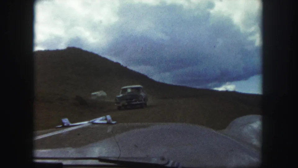A classic automobile travels ahead on a Colorado Springs dirt road, filmed from inside another moving car.