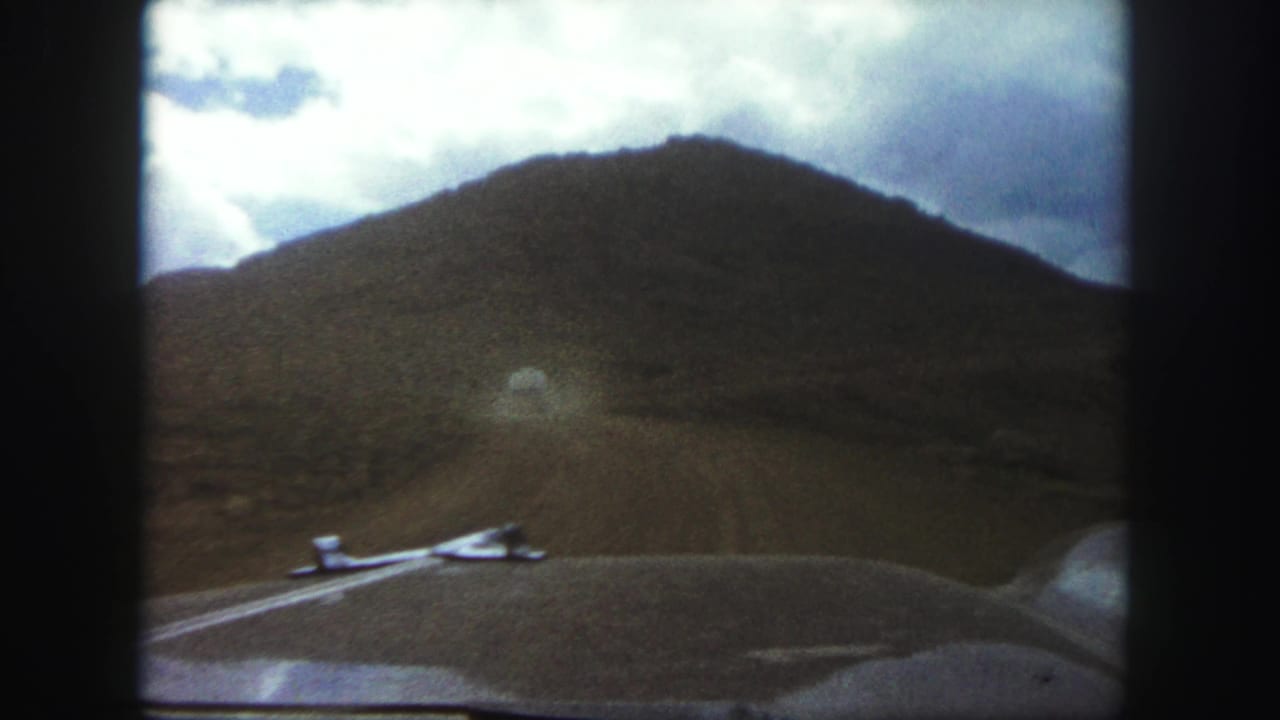 Windshield view of a dirt road running toward a hill, with car hood in front.