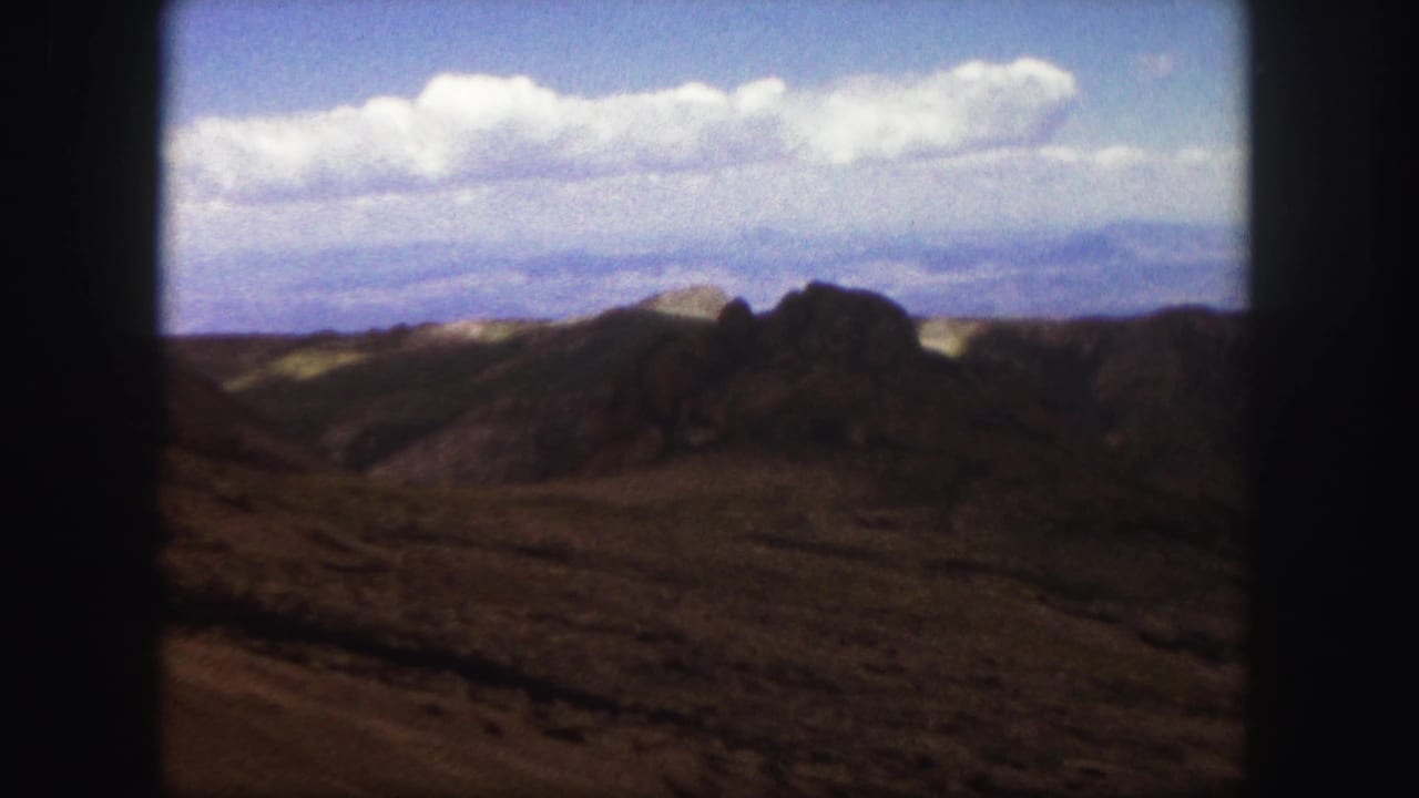1958 Colorado Springs landscape frame with rugged rock formations, low hills, and a cloud band across the sky.