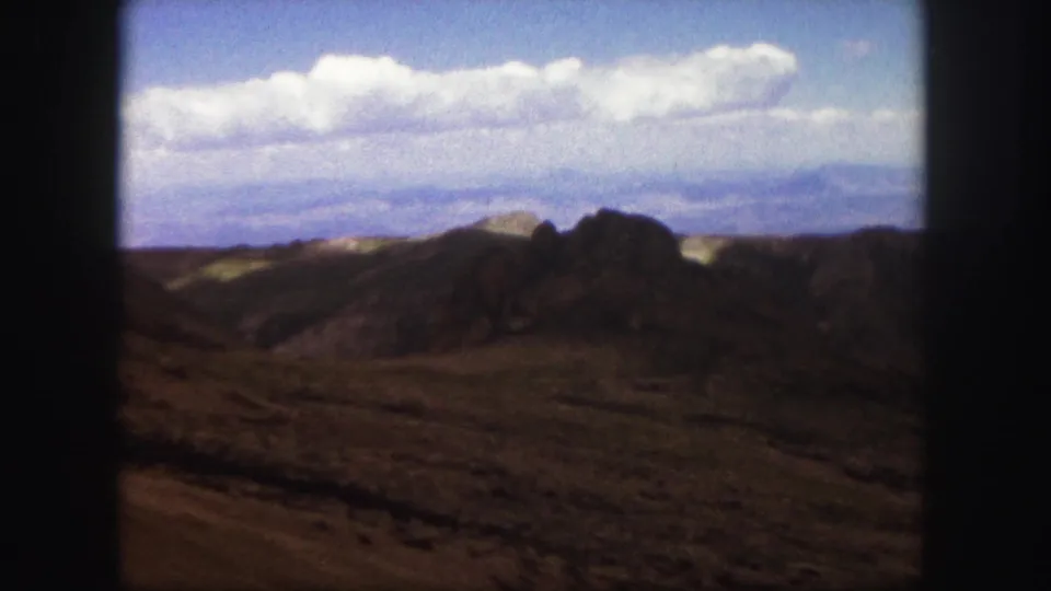1958 Colorado Springs landscape frame with rugged rock formations, low hills, and a cloud band across the sky.
