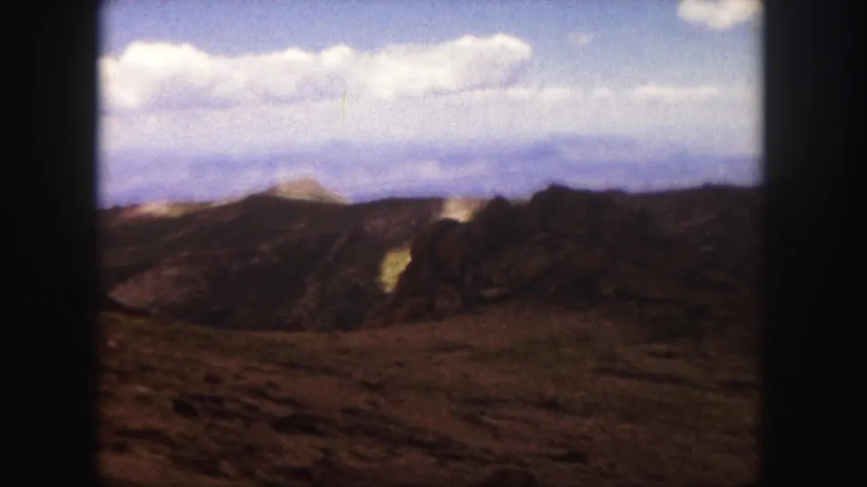 1958 Colorado Springs frame showing rocky hillside terrain, distant blue mountains, white clouds, and soft 8mm color.