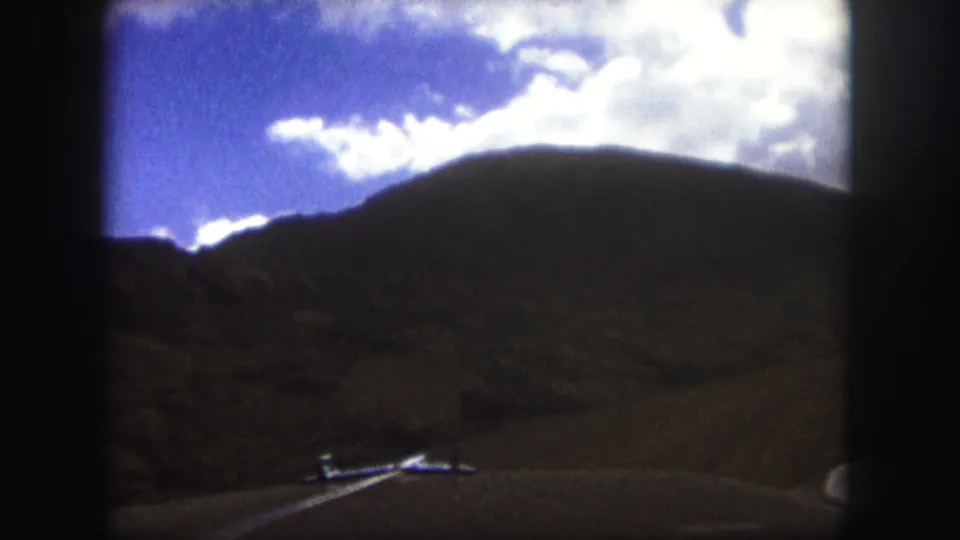 1958 road-trip view near Colorado Springs, showing a winding paved road, hills, and a small distant car.