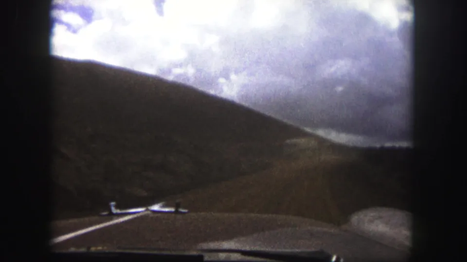 Colorado Springs 1958 car-window view showing a dirt road beside a dark hillside, with the hood and windshield edges visible in the foreground.