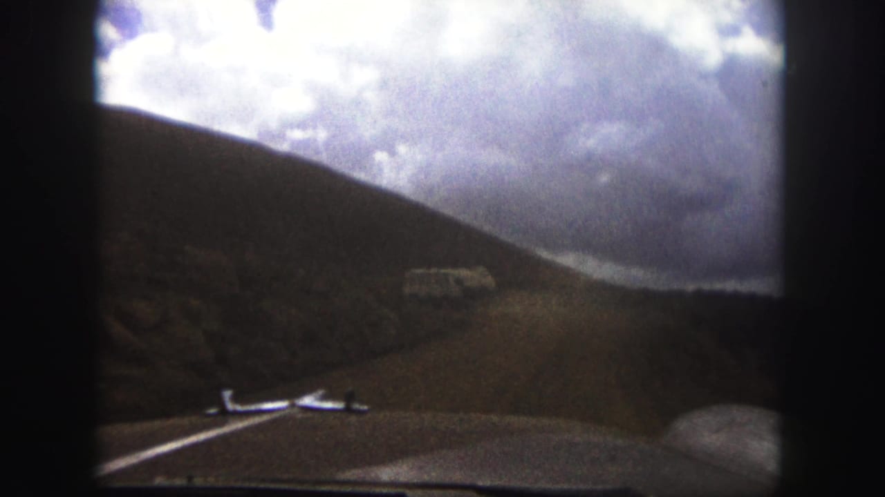 1958 Colorado Springs 8mm travel view from inside a vehicle, showing a dirt mountain road, hillside, dashboard, and white bus ahead.