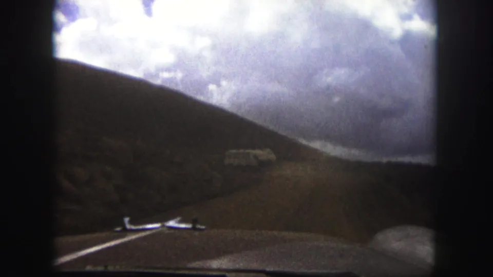 1958 Colorado Springs 8mm travel view from inside a vehicle, showing a dirt mountain road, hillside, dashboard, and white bus ahead.