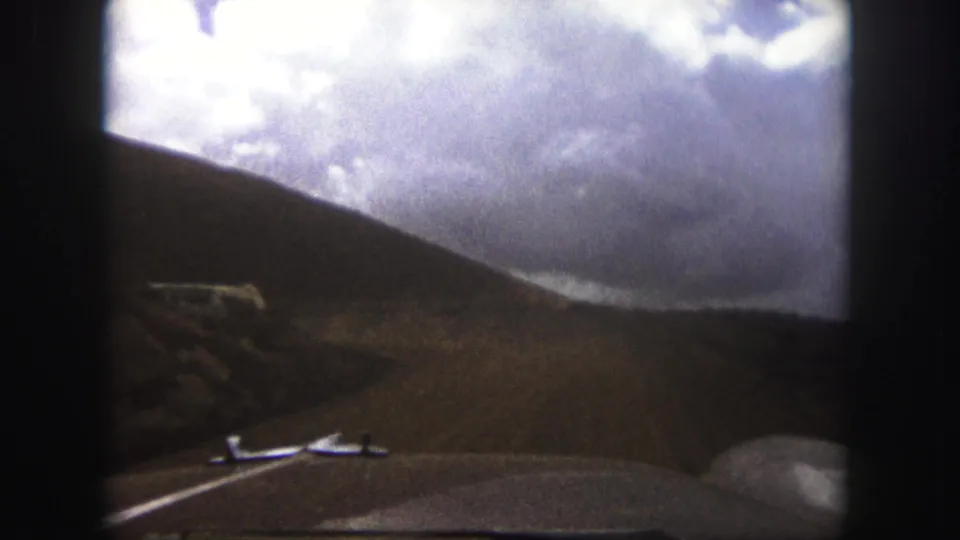 1958 Colorado Springs home-movie frame showing a windshield view of dusty road travel through hills with a bus ahead.