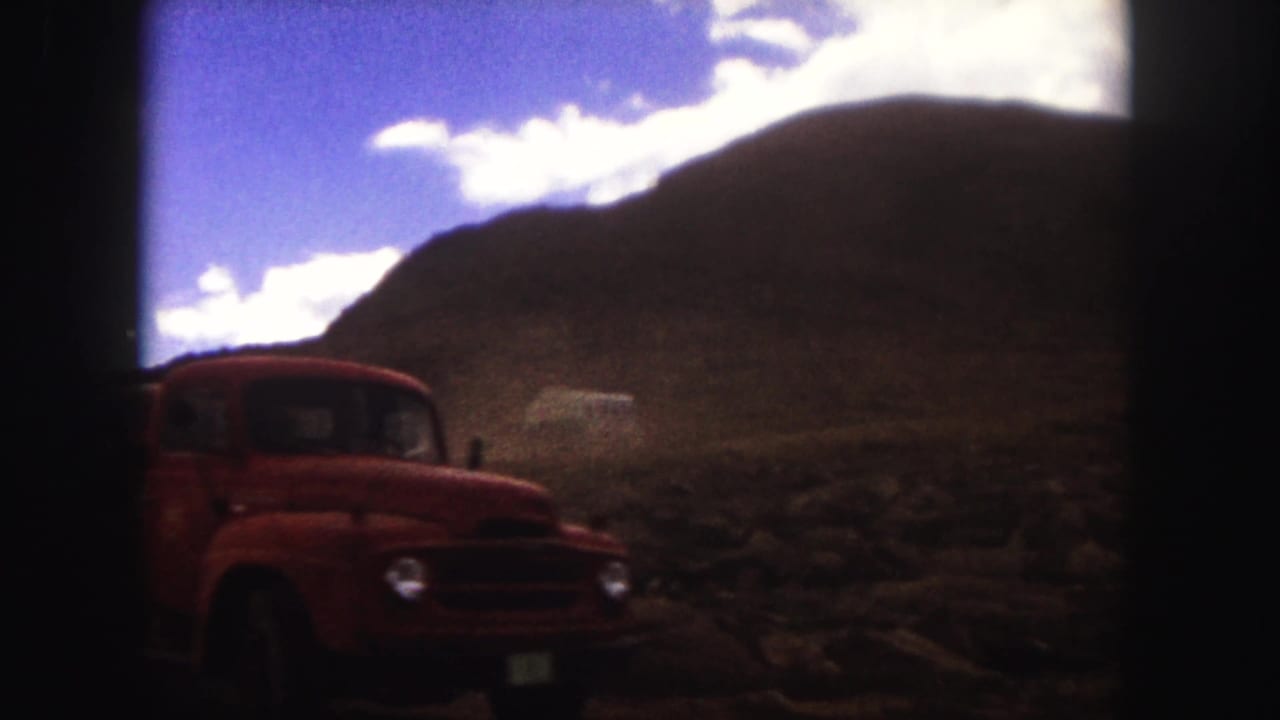 Red vintage truck passing close to the camera on a dusty road.