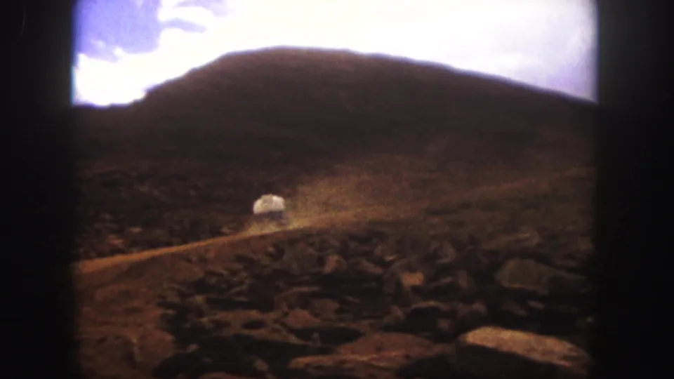 1958 Colorado Springs 8mm frame showing dust hanging over a winding dirt road in a rocky mountain landscape after the truck passes.