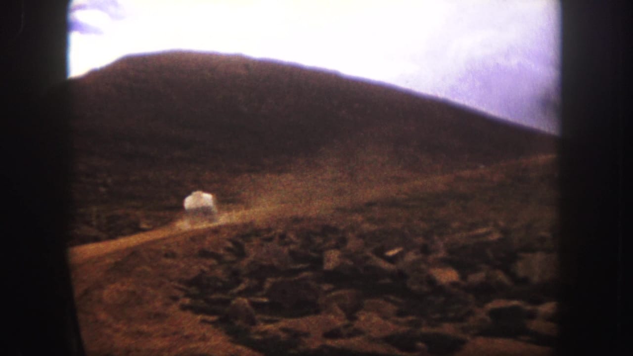1958 Colorado Springs road-trip footage showing a white car climbing a dusty dirt road beneath a rocky mountain hillside.