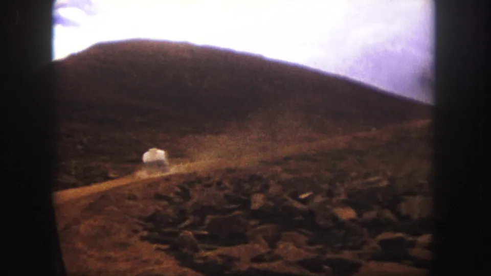 1958 Colorado Springs road-trip footage showing a white car climbing a dusty dirt road beneath a rocky mountain hillside.
