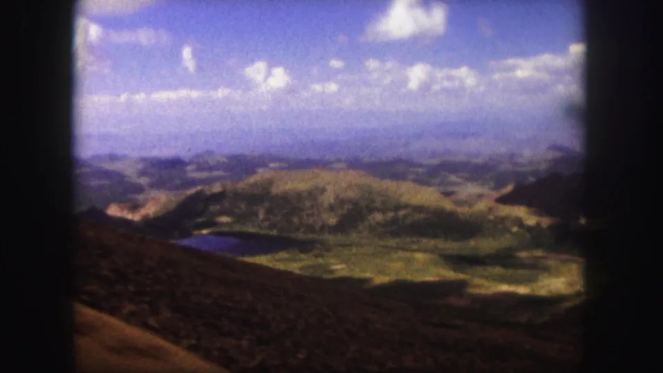 A 1958 home-movie view near Colorado Springs looking over rolling hills, a small lake, distant valley, and blue sky.