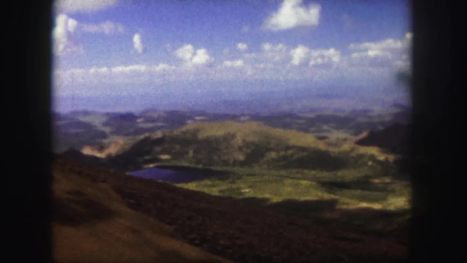 Scenic Colorado Springs area overlook with green hills, a small body of water, distant terrain, and bright clouded sky on 8mm film.