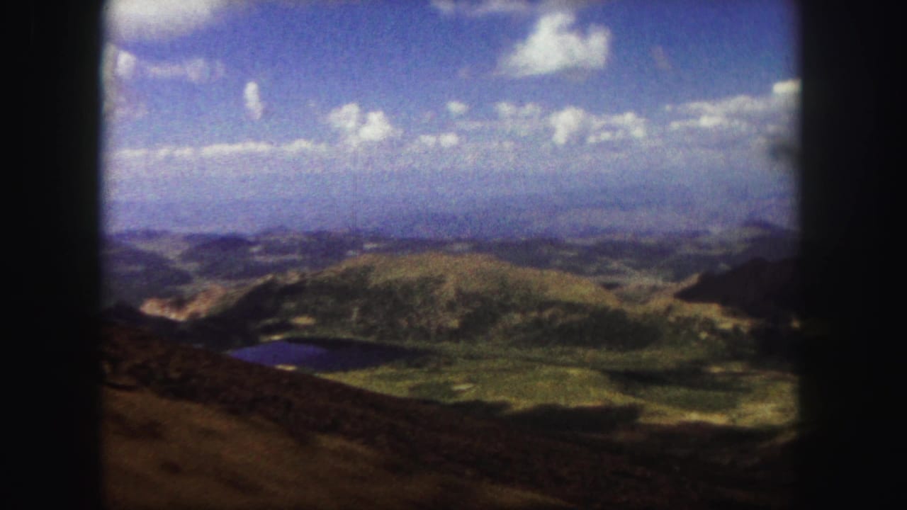 1958 Colorado Springs landscape view with rounded 8mm frame edges, showing a lake below green hills and a cloud-dotted sky.
