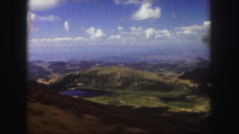 1958 Colorado Springs landscape view with rounded 8mm frame edges, showing a lake below green hills and a cloud-dotted sky.