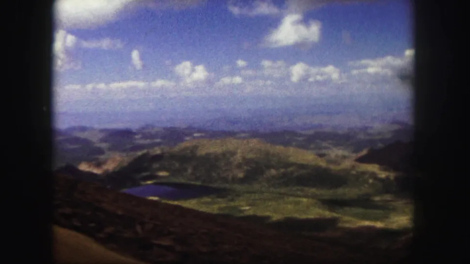 Colorado Springs 1958 8mm frame from a high overlook, with green terrain, a dark lake, distant hills, and visible film grain.