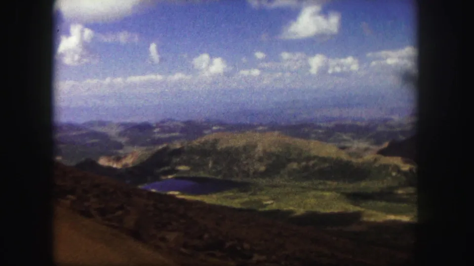 Colorado Springs travel footage frame showing rounded mountain terrain, a valley lake, and scattered clouds in soft 8mm color.