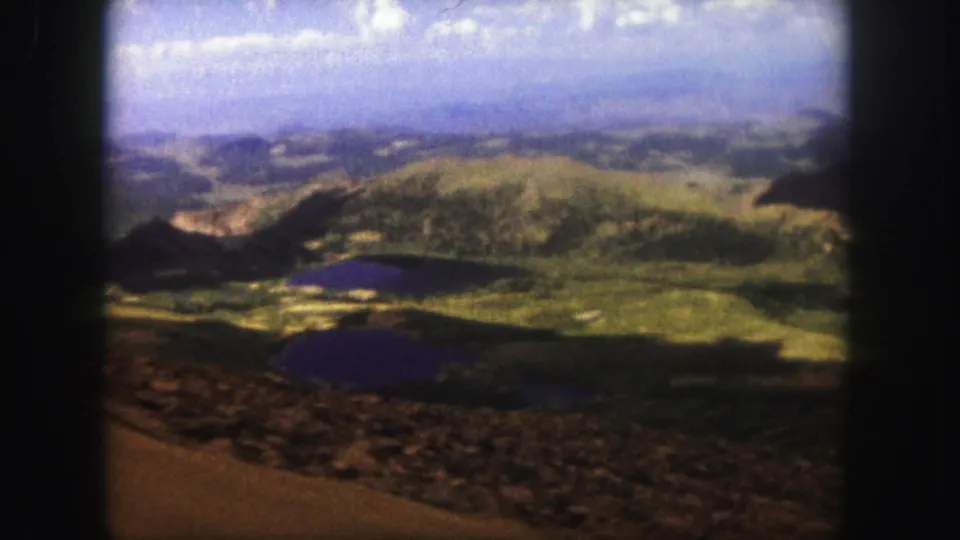 1958 8mm Colorado Springs landscape frame with two dark lakes below green hills and a rocky high-altitude foreground.