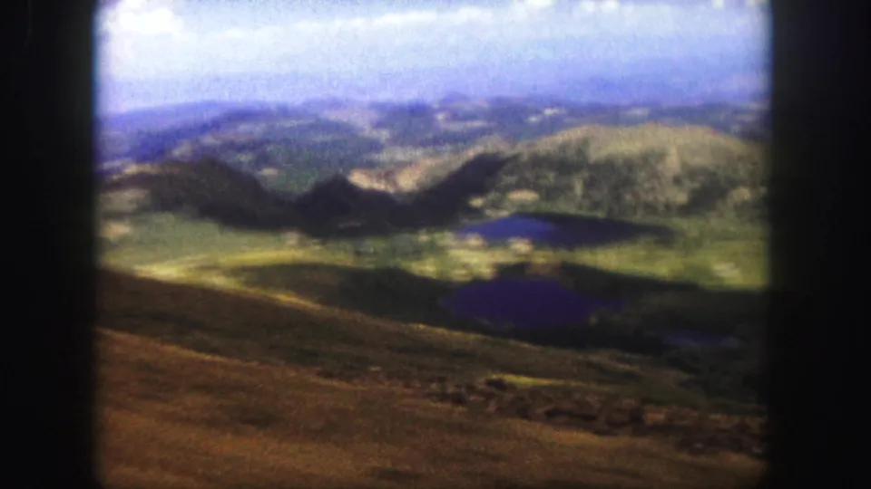 Final 1958 Colorado Springs frame looking over brown ridge terrain toward green hills, small dark lakes, and a hazy horizon.