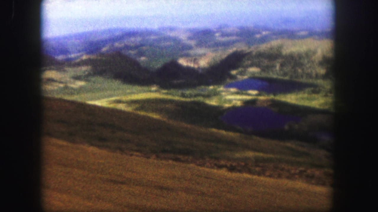 Elevated 1958 Colorado Springs-area view of rolling mountain terrain, dark ridges, and small reflective lakes on faded 8mm film.