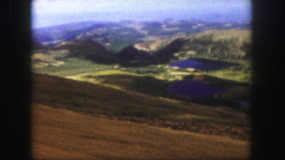 Elevated 1958 Colorado Springs-area view of rolling mountain terrain, dark ridges, and small reflective lakes on faded 8mm film.