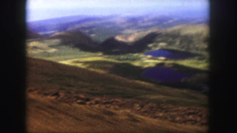 A blurred 8mm frame from the 1958 Colorado Springs-area clip shows a brown slope dropping toward lakes and distant mountain forms.