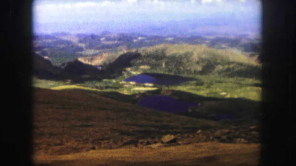 1958 8mm view from Pikes Peak over Colorado ridges and alpine lakes, framed with soft focus and visible home-movie grain.