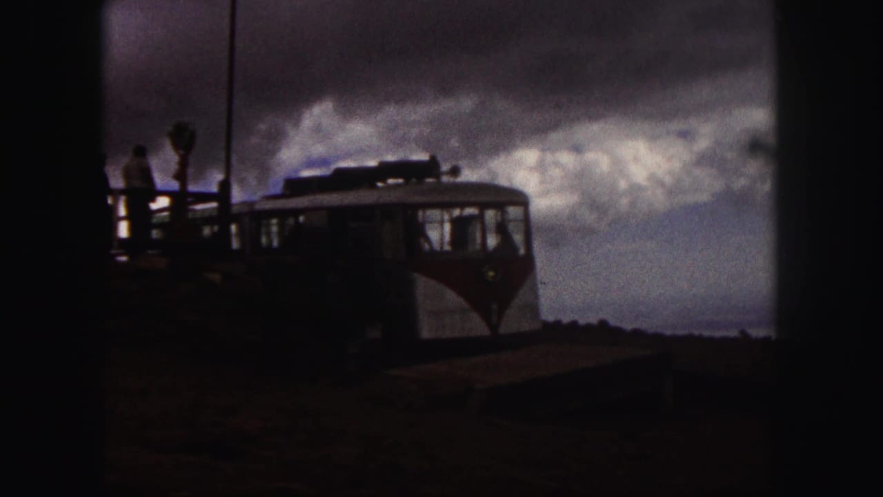 Tourist vehicle beside a platform under a cloudy mountain sky.