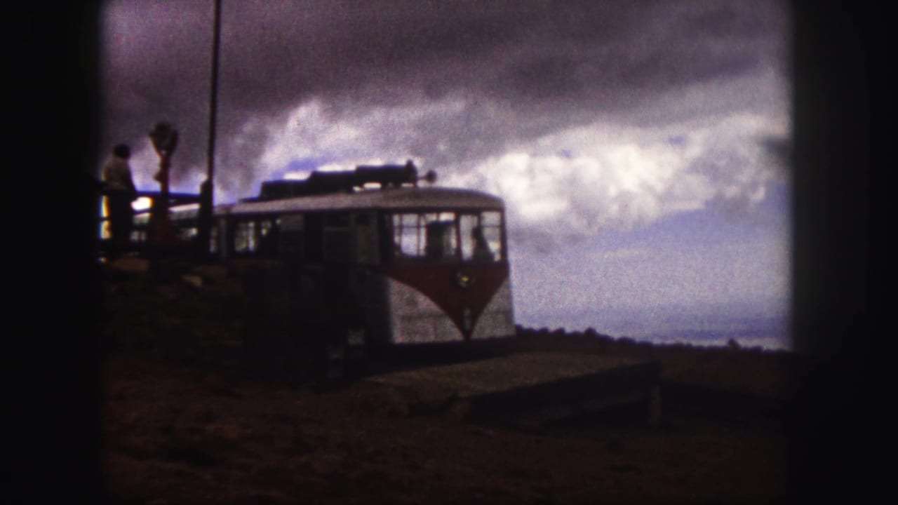 A red-and-white sightseeing vehicle stands near a platform with visitors in 1958 Pikes Peak home-movie footage.
