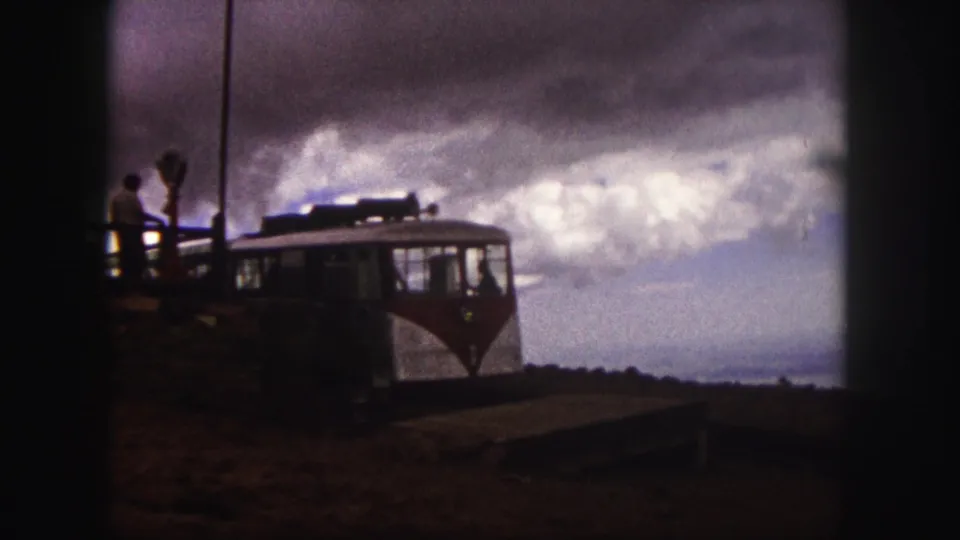 A Pikes Peak tourist vehicle remains beside the platform while visitors stand nearby in grainy 1958 8mm footage.