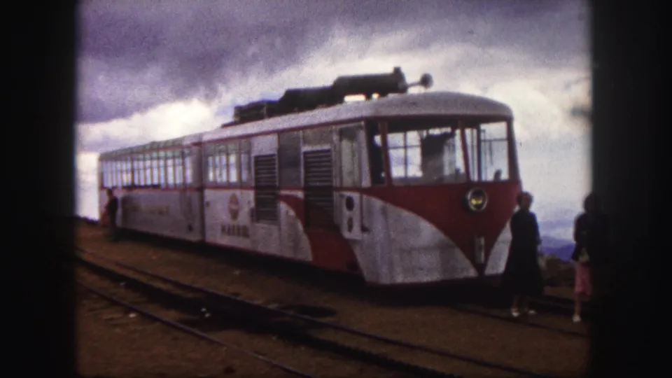 Colorado Springs 1958 frame of a red-and-white mountain train at the station, with passengers near the front and rails in the foreground.