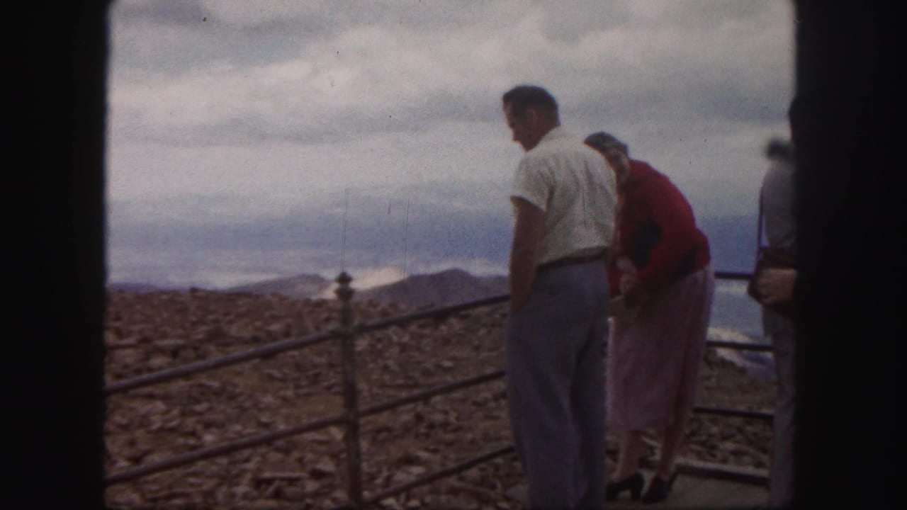 1958 Colorado Springs home-movie frame showing two tourists at a mountain overlook under a cloudy sky.