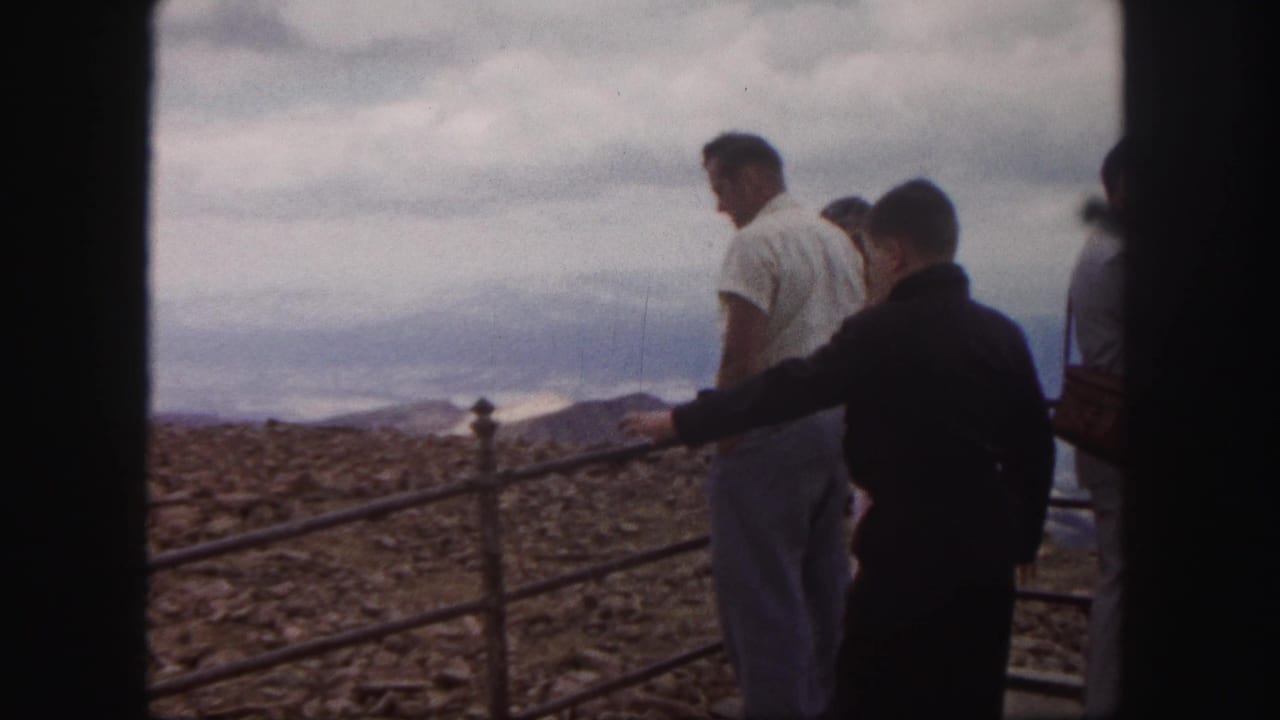 A boy enters beside two adults at the railing, pointing toward the mountain view.