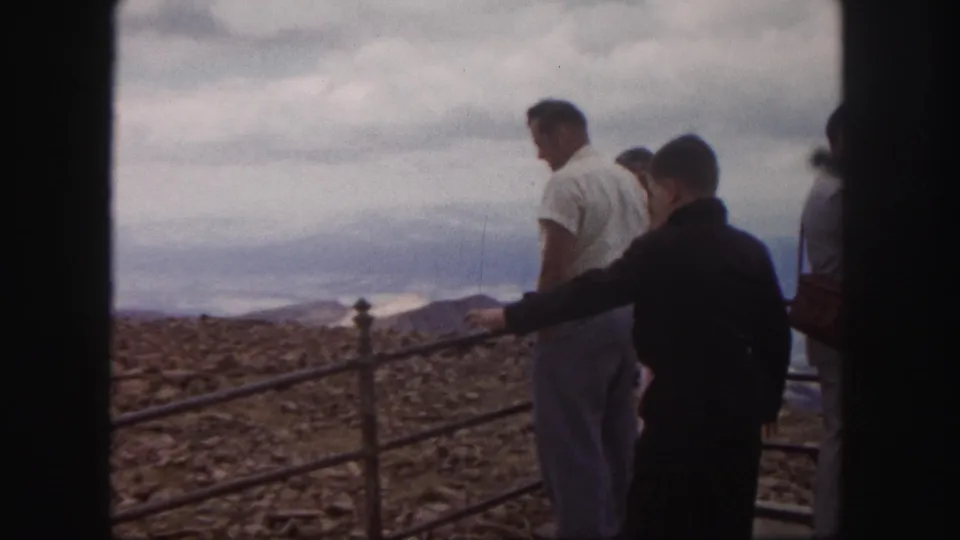 1958 Colorado Springs frame with a boy and adults at a scenic railing overlooking distant mountains.