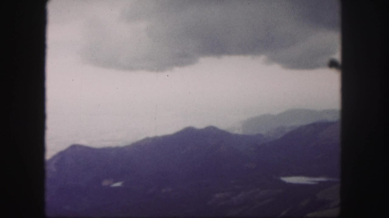 Distant mountain range and small lake seen through dark film-frame edges.