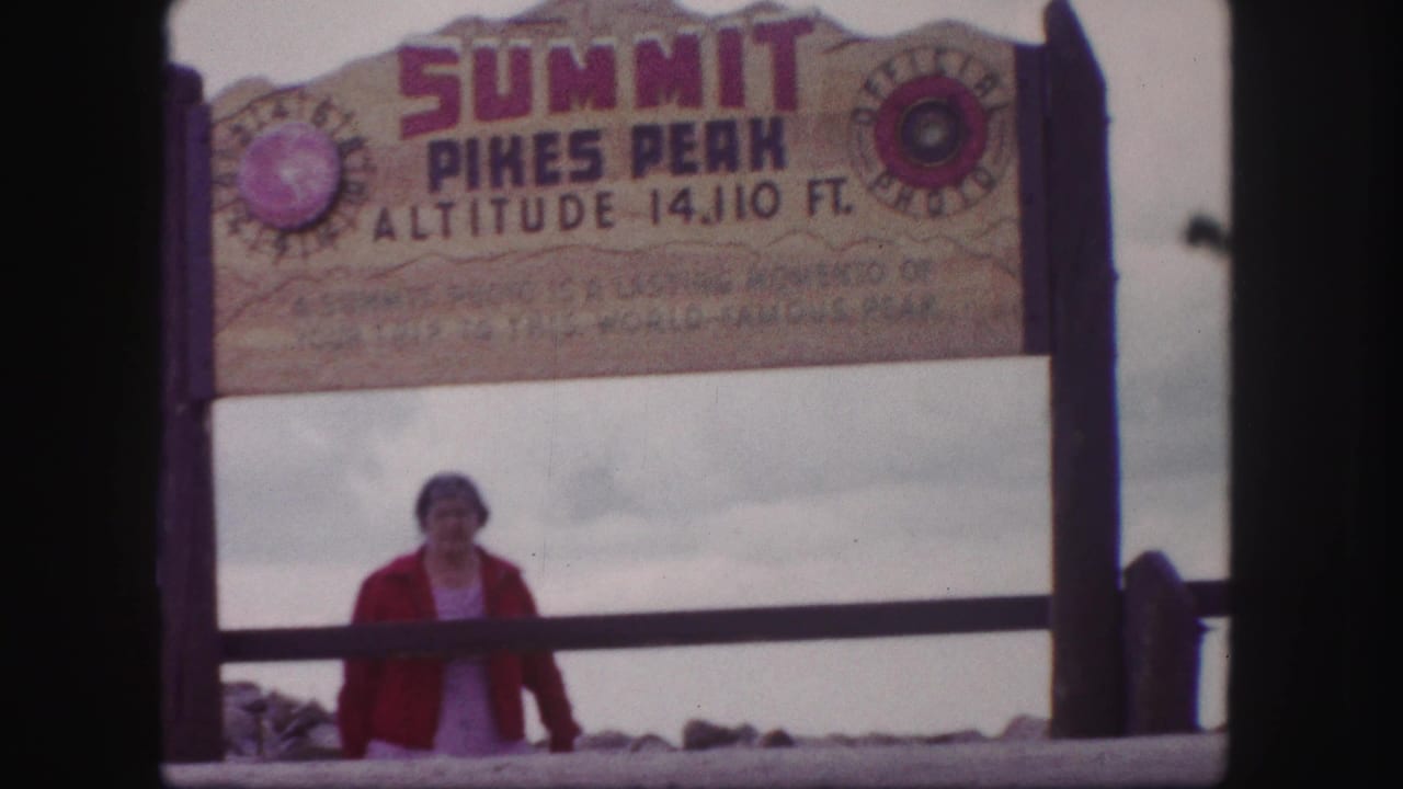 1958 Colorado Springs home-movie frame showing a woman below the Pikes Peak summit altitude sign.