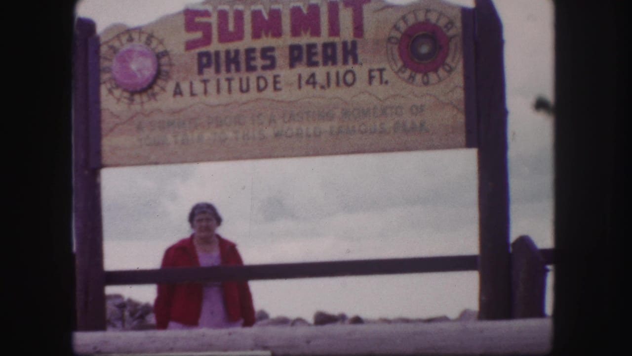 Woman centered below a summit sign reading Pikes Peak altitude 14,110 ft.