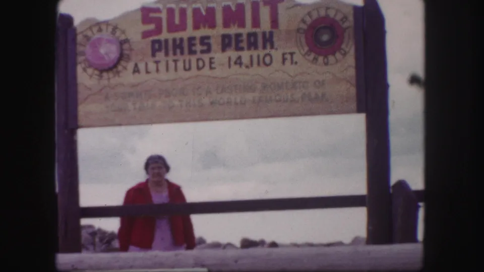 Colorado Springs summit scene with a woman standing under the Pikes Peak 14,110-foot sign.