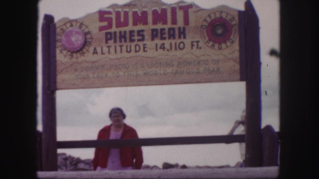 1958 Pikes Peak summit frame showing the woman under the sign and a partial figure entering at right.
