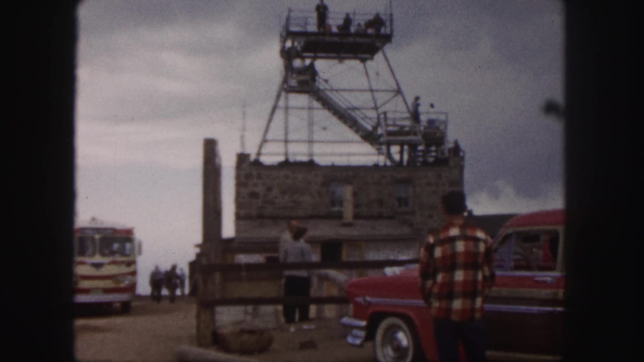A summit-area stone building and metal observation tower are shown with visitors, a vintage bus, and a red car in 1958 footage.