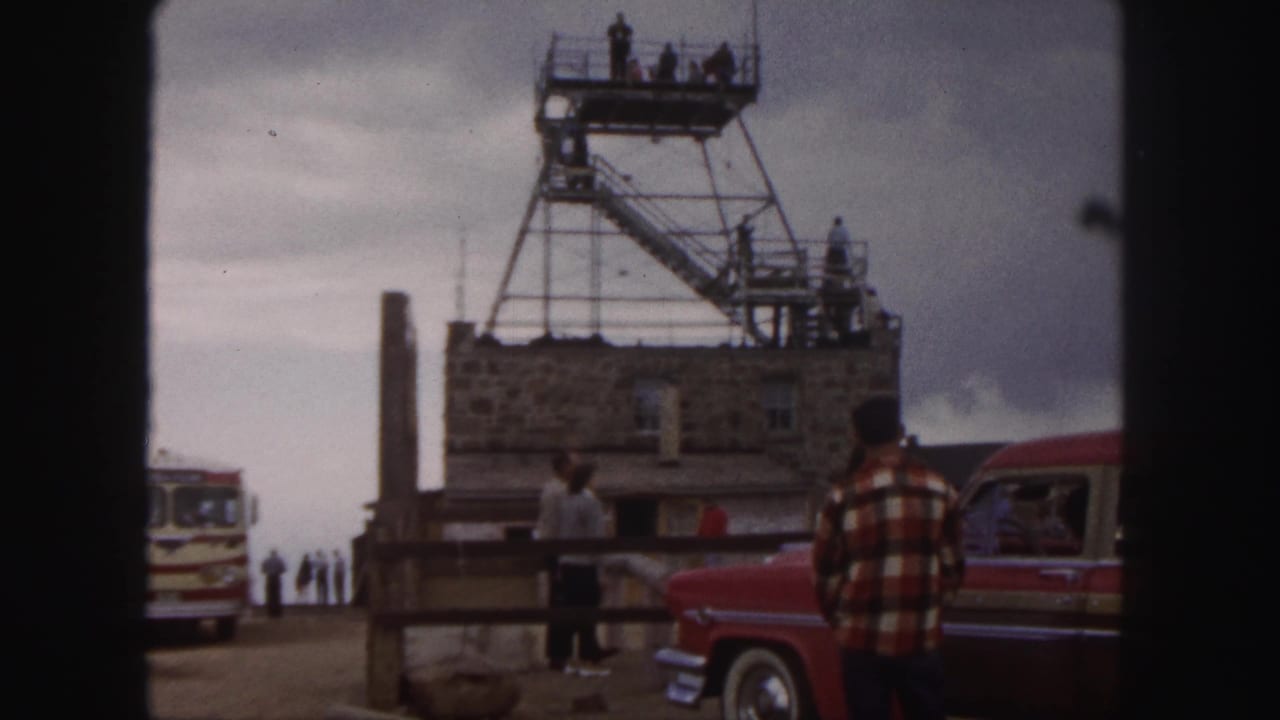 1958 Colorado Springs overlook view with visitors near a stone structure, metal tower stairs, red car, and tour bus.
