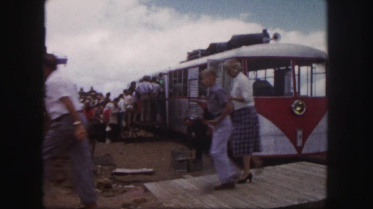 1958 Colorado Springs home-movie frame showing tourists near a red and white mountain transport car as people board from a stone platform.