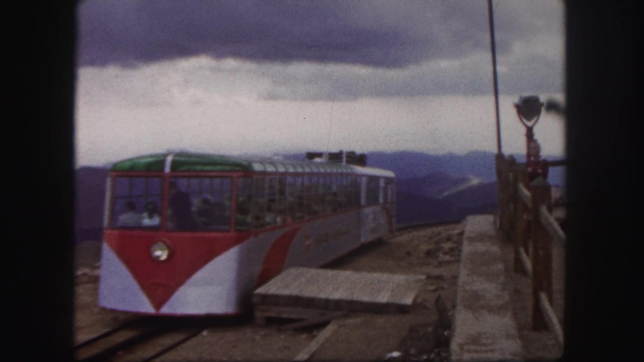 1958 Colorado Springs frame of a red-and-white mountain railway car approaching the platform with passengers visible through the windows.