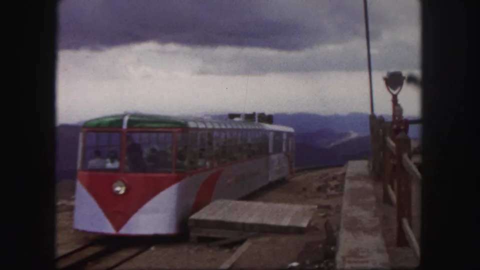 1958 Colorado Springs frame of a red-and-white mountain railway car approaching the platform with passengers visible through the windows.