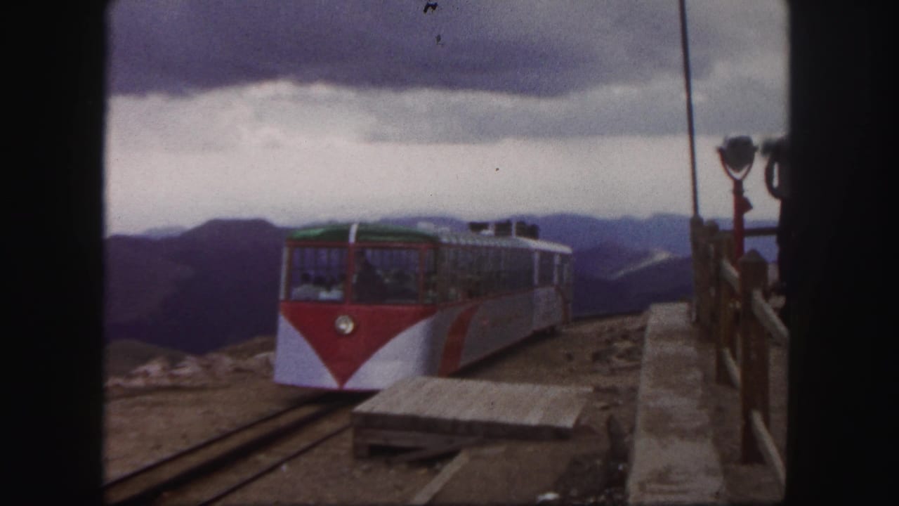 1958 Colorado Springs 8mm view of a mountain railway car arriving at a station platform with distant ridges under heavy clouds.