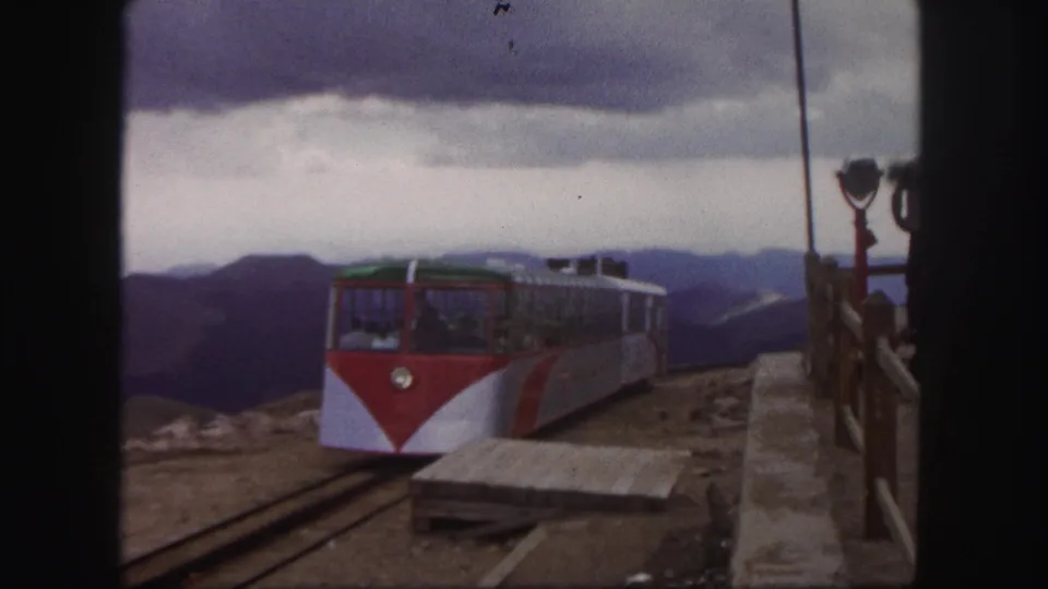 1958 Colorado Springs 8mm view of a mountain railway car arriving at a station platform with distant ridges under heavy clouds.